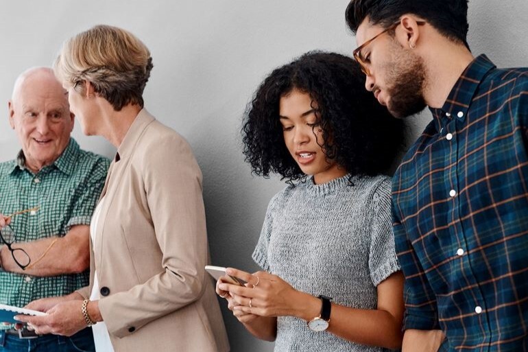 A group of colleagues of varying ages chatting against a plain wall.